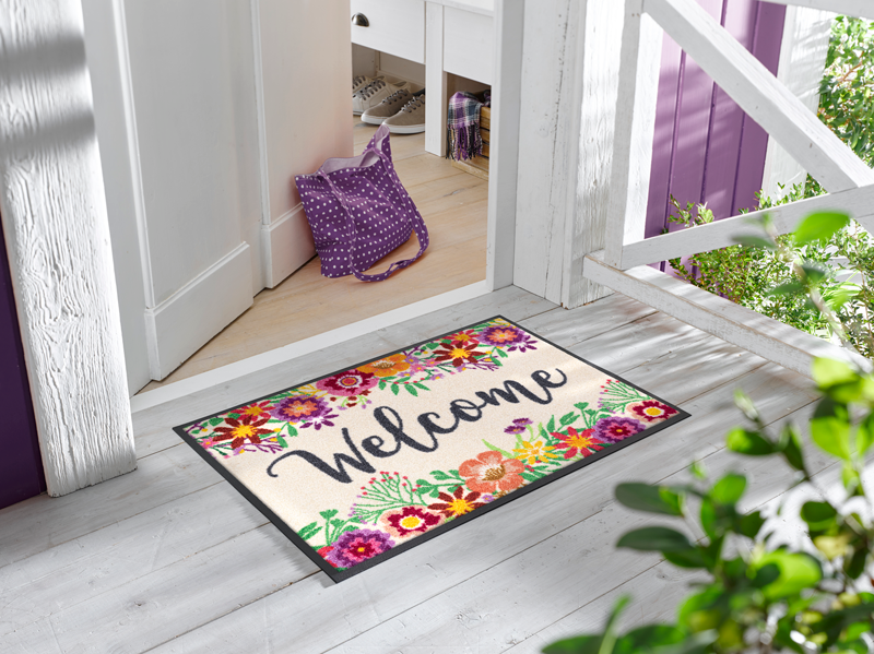 Fußmatte mit Blumen und Schriftzug "Welcome" vor der Haustür