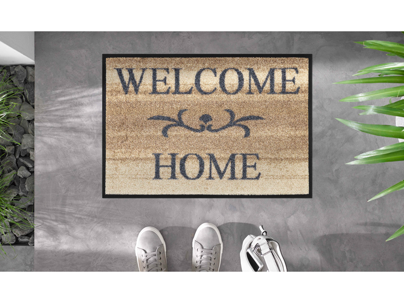 hellbraune Fußmatte mit Ornament und Schriftzug "WELCOME HOME" auf dem Fußboden